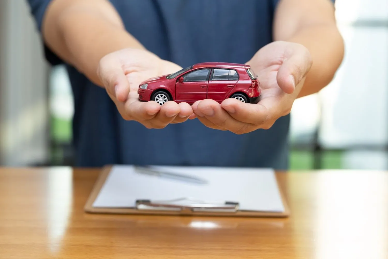 Hands holding a small red toy car over a clipboard